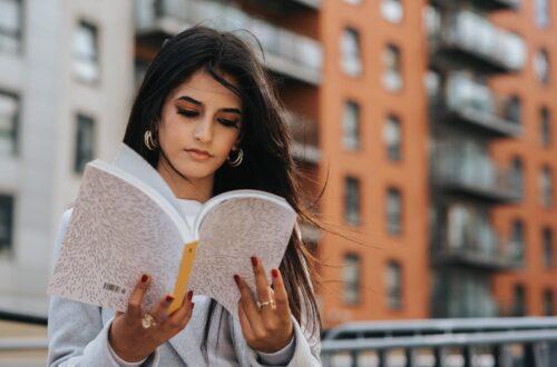 focused ethnic woman reading magazine in city